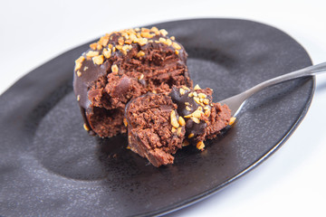 Rum ball decorated with chocolate and nuts on a black plate eaten with a fork on a white background