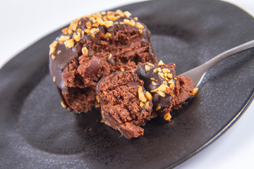 Rum ball decorated with chocolate and nuts on a black plate eaten with a fork on a white background