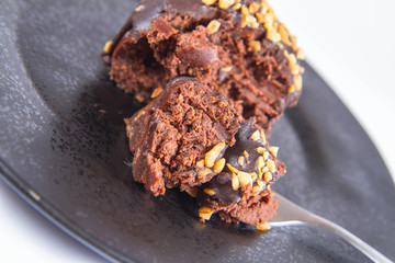 Rum ball decorated with chocolate and nuts on a black plate eaten with a fork on a white background