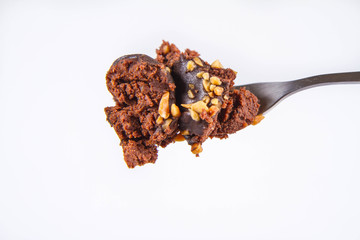 Rum ball decorated with chocolate and nuts on a fork on a white background