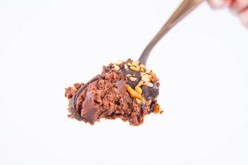 Rum ball decorated with chocolate and nuts on a fork on a white background