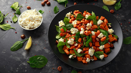 Healthy roasted sweet potato salad with spinach, feta cheese, hazelnut nuts in black plate
