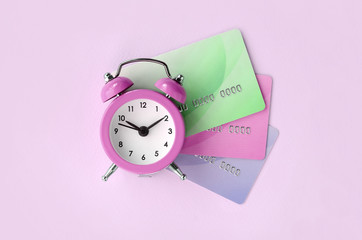 Small pink alarm clock lies on colored credit cards. The concept of modern fast online banking and...