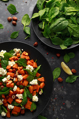 Healthy roasted sweet potato salad with spinach, feta cheese, hazelnut nuts in black plate