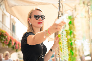 joung beautiful blond woman on the market are looking for some gifs, sunglasses and bags. she is shopping on a sunny day in italy on her travel