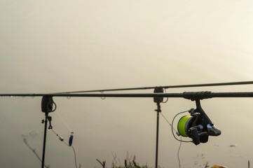 Carp fishing rod with a coil in the foreground and a bite alarm on the morning dawn in anticipation of a bite of fish.