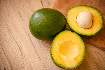 A whole and Halves of Green Fresh Avocado on wooden background.