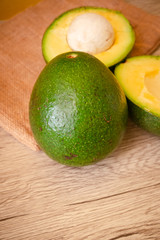 A whole and Halves of Green Fresh Avocado on wooden background.