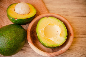 A whole and A Half of Green Fresh Avocado on wooden background. The other half in the wood bowl