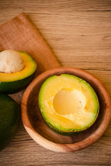 A whole and A Half of Green Fresh Avocado on wooden background. The other half in the wood bowl