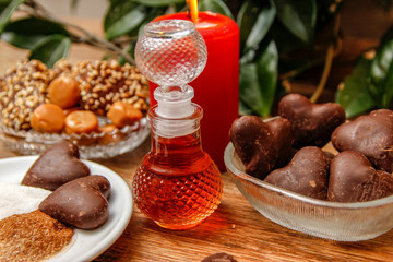 Bottle of perfume and various of cookies on wooden table with red candle. Home liana in the background. Close up.