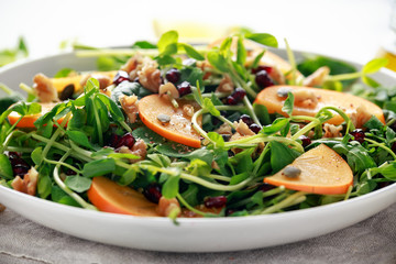 Tasty Persimmon and pea shoot salad with walnuts, pomegranate and pumpkin seed in a white plate