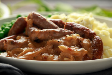 Mashed potatoes and sausages, bangers with onions gravy, green peas. close up