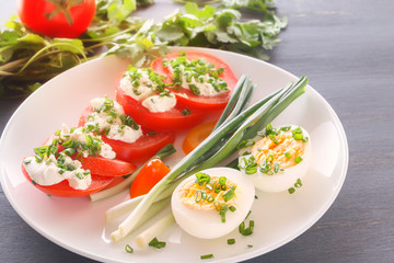 Half boiled eggs with tomatoes, green onions sprinkled with greens in a white plate on a gray wooden table. Close-up