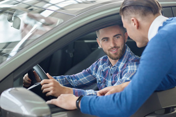 Young man in blue sweater helping his friend choosing auto.