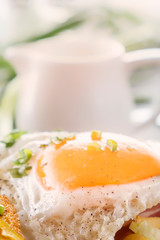 Fried egg with bacon in a plate with fried pieces of bread, greens and french fries on a gray wooden table. Close-up