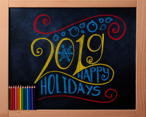Happy Holidays 2019 colorful chalk lettering on blackboard with pencils