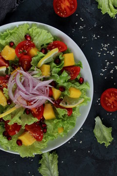 Fresh salad with lettuce, mango, tomato, onion, sesame and pomegranate. Diet food. Top view. Vegetarian and vegan food.