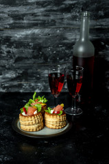 French cuisine, crunchy patties with lettuce and smoked salmon on a dark, rustic background, next to a glass of red wine