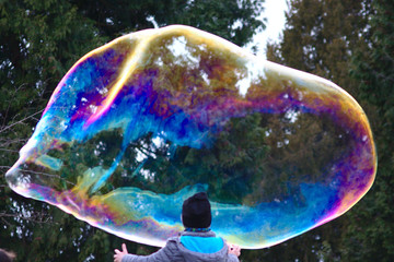 Gigantische Seifenblase schillert wie ein Regenbogen in prächtigen Farben im Sonnenschein