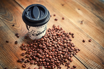 cardboard coffee cup with plastic lid and roasted coffee beans on wooden background