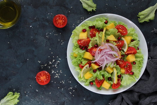 Fresh salad with lettuce, mango, tomato, onion, sesame and pomegranate. Diet food. Top view. Vegetarian and vegan food.