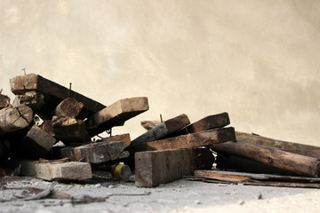Hosue construction site details of a pile of used wooden planks with nails sticking out with a plain concrete wall background