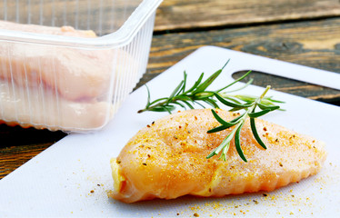 Uncooked Chicken breast with steak seasoning powder and rosemary on plastic cutting boards.