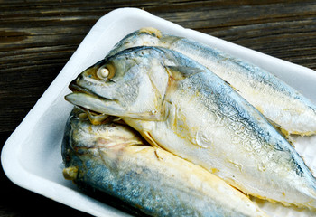 Mackerel steamed on foam tray with wooden background.