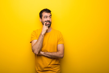 Man on isolated vibrant yellow color having doubts while looking up