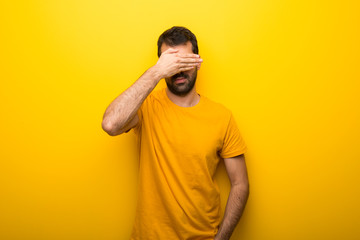 Man on isolated vibrant yellow color covering eyes by hands. Do not want to see something