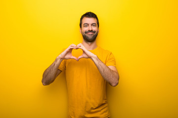 Man on isolated vibrant yellow color making heart symbol by hands