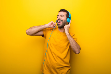 Man on isolated vibrant yellow color listening to music with headphones