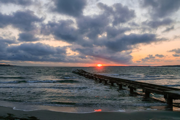 seascape with romantic pier, clouds and waves at sunrise