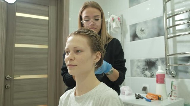 woman hairdresser colorist at home in the bathroom puts paint on the hair of a young woman, applies paint with a brush on the hair, beauty, fashion