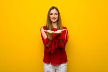 Young girl with red dress over yellow wall holding copyspace imaginary on the palm to insert an ad