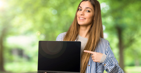 Fototapeta premium Young girl with striped shirt showing a laptop at outdoors