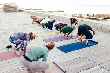 Group of positive sporty people practicing various yoga positions during training on beach at...