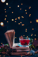 Red berry tea on a stack of books with fairy lights. Christmas drink on a dark background with copy...