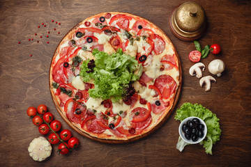 Pizza with ham, salami, cheese, mushrooms, cherry tomatoes, bell peppers and salad on a wooden brown board.