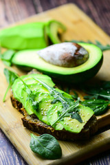 Spinacia oleracea, Eruca sativa. Toast with avocado on rustic wooden background. Avocado sandwich with ingredients. Selection of healthy food for heart, life concept.