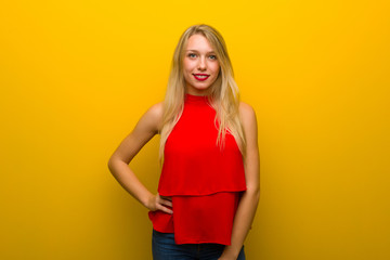 Young girl with red dress over yellow wall posing with arms at hip and smiling