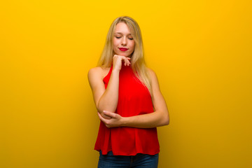 Young girl with red dress over yellow wall looking down with the hand on the chin