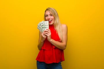 Young girl with red dress over yellow wall taking a lot of money