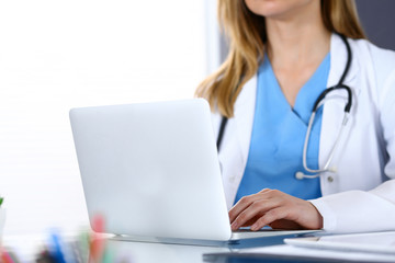 Doctor typing on laptop computer while sitting at the glass desk in hospital office. Physician at work. Medicine and healthcare concept