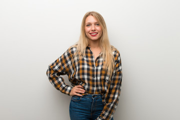 Blonde young girl over white wall posing with arms at hip and smiling