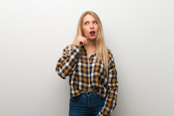 Blonde young girl over white wall thinking an idea pointing the finger up