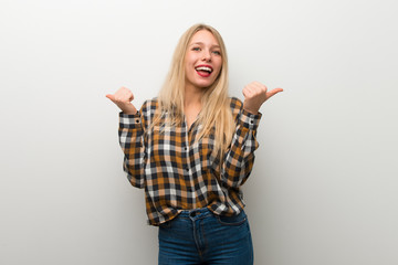 Blonde young girl over white wall giving a thumbs up gesture with both hands and smiling