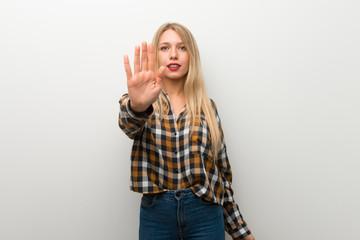 Blonde young girl over white wall making stop gesture denying a situation that thinks wrong