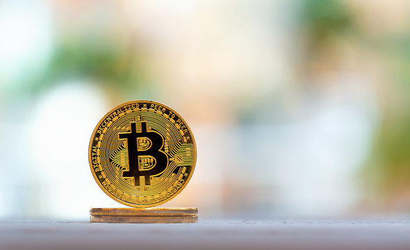 A gold bitcoin cryptocurrency coin on a bright interior room background
